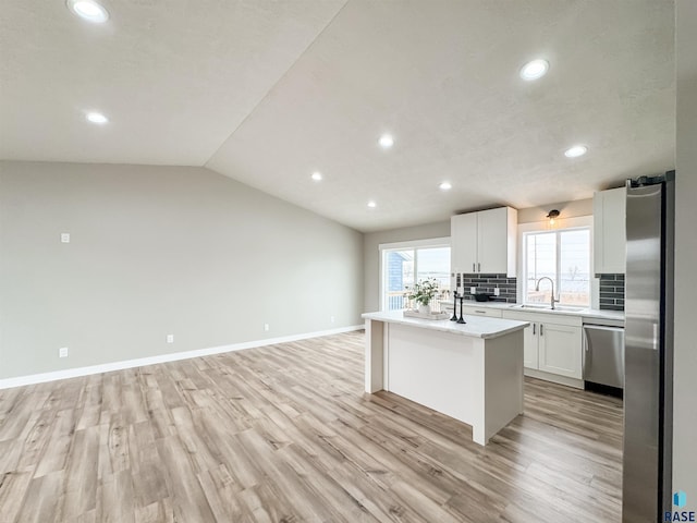 kitchen featuring light countertops, tasteful backsplash, appliances with stainless steel finishes, a sink, and light wood-type flooring