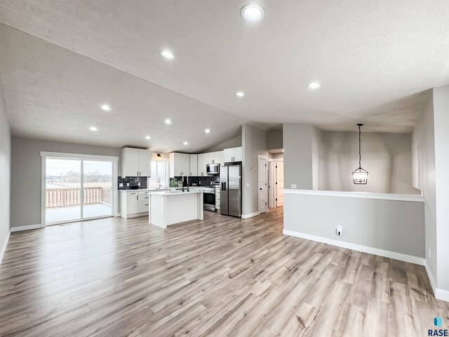 kitchen with appliances with stainless steel finishes, white cabinetry, light wood-type flooring, open floor plan, and a center island