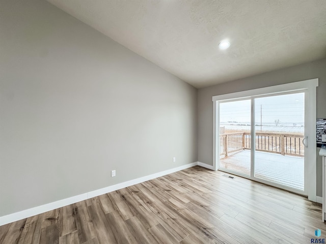 unfurnished room with baseboards, light wood-style floors, vaulted ceiling, and visible vents