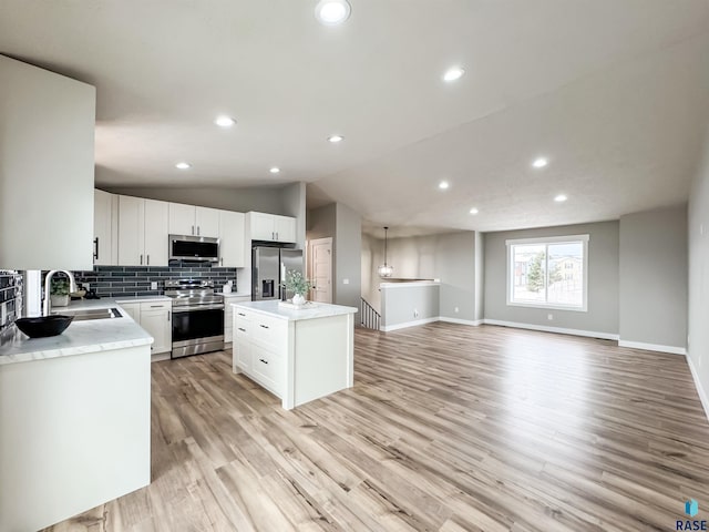 kitchen with decorative backsplash, light wood-style flooring, stainless steel appliances, a kitchen island, and a sink
