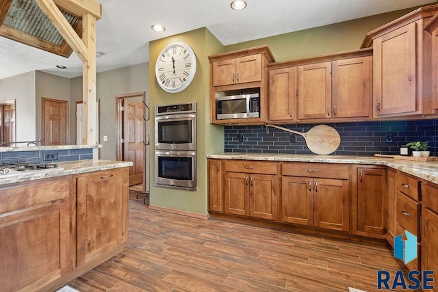 kitchen with brown cabinetry, wood finished floors, decorative backsplash, and stainless steel appliances