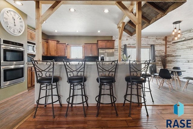 kitchen with a kitchen bar, stainless steel appliances, dark wood-type flooring, and brown cabinetry