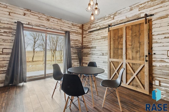dining area featuring a barn door, wood finished floors, and wood walls