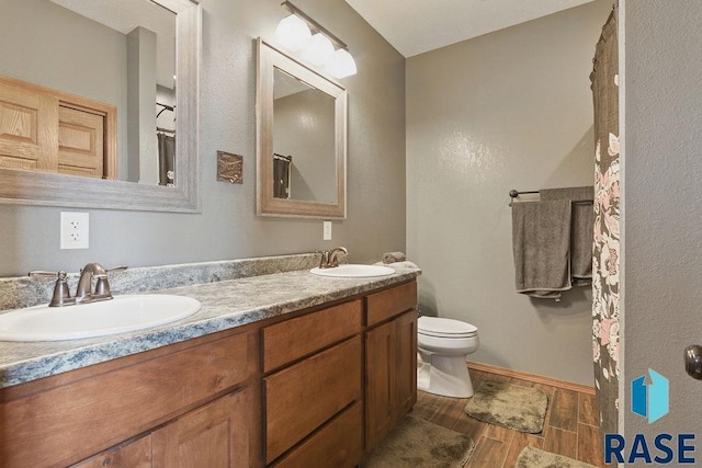 bathroom featuring wood tiled floor, a sink, toilet, and double vanity