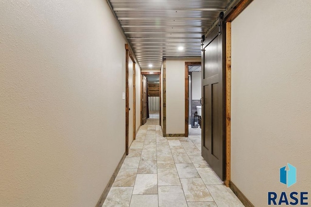 corridor featuring baseboards, a barn door, and a textured wall