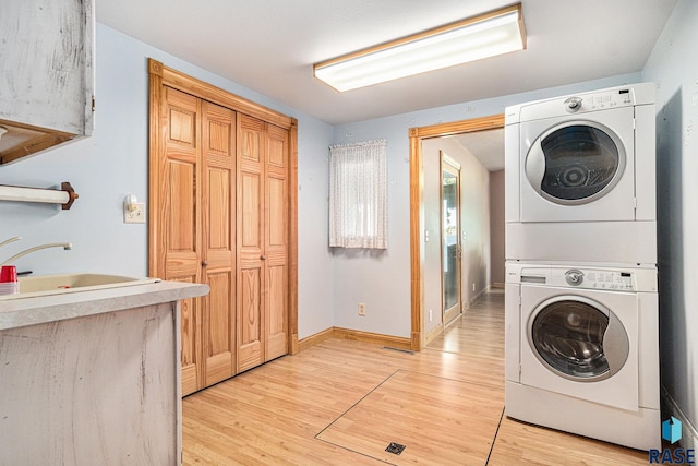 washroom with baseboards, stacked washer / drying machine, laundry area, a sink, and light wood-type flooring