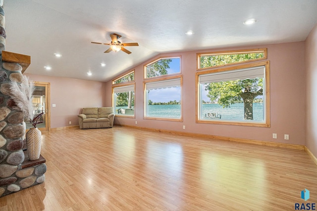 living area with vaulted ceiling, a stone fireplace, baseboards, light wood-style floors, and ceiling fan