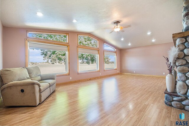 living room featuring a textured ceiling, a fireplace, a ceiling fan, lofted ceiling, and light wood-type flooring
