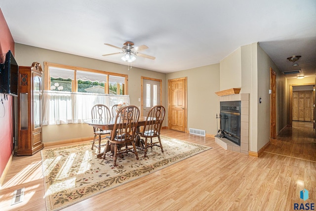 dining room with light wood finished floors, visible vents, a tile fireplace, and a ceiling fan