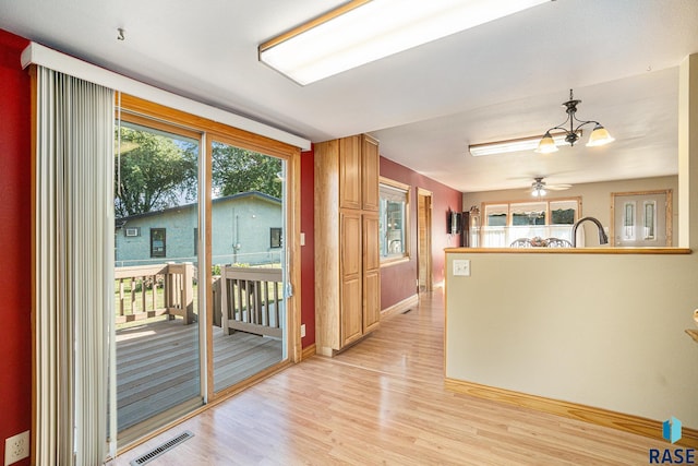 doorway to outside with light wood-type flooring, ceiling fan with notable chandelier, baseboards, and visible vents