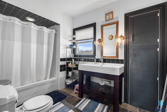full bathroom featuring toilet, vanity, tile walls, stone finish flooring, and shower / tub combo