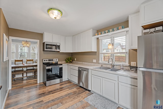 kitchen with light countertops, stainless steel appliances, a sink, light wood-style floors, and white cabinets