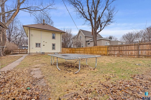 rear view of property with a fenced backyard, a yard, a chimney, and a trampoline