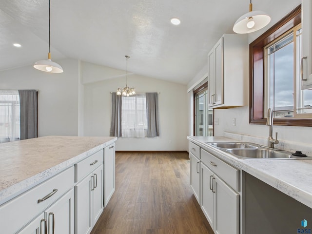 kitchen with light countertops, decorative light fixtures, vaulted ceiling, a sink, and dark wood-style floors