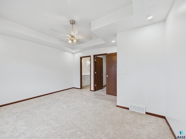 unfurnished room with visible vents, baseboards, a ceiling fan, a raised ceiling, and light colored carpet