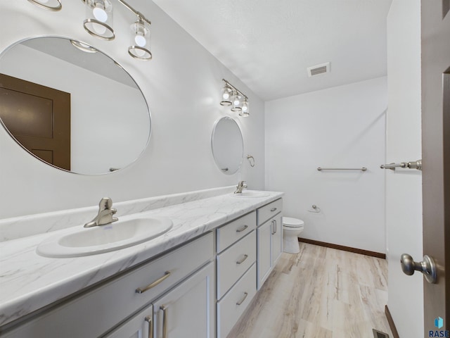 bathroom featuring toilet, a sink, double vanity, and wood finished floors