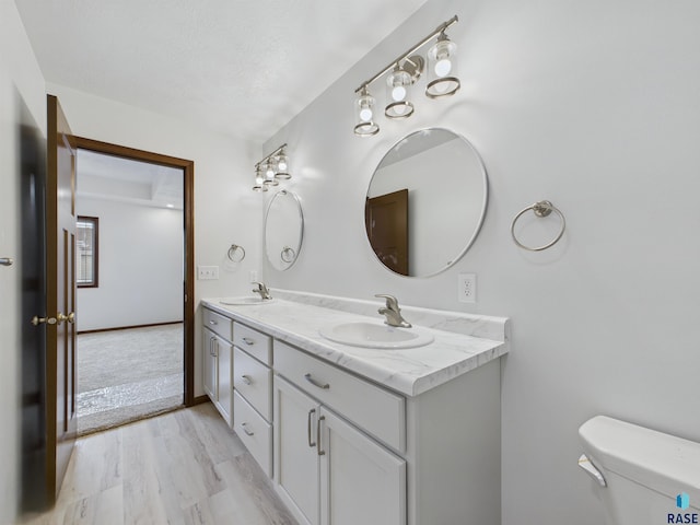 full bathroom featuring double vanity, a sink, toilet, and wood finished floors