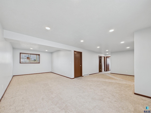 basement featuring light carpet, a textured ceiling, baseboards, visible vents, and recessed lighting