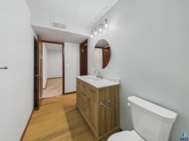 bathroom with vanity, toilet, baseboards, visible vents, and wood finished floors