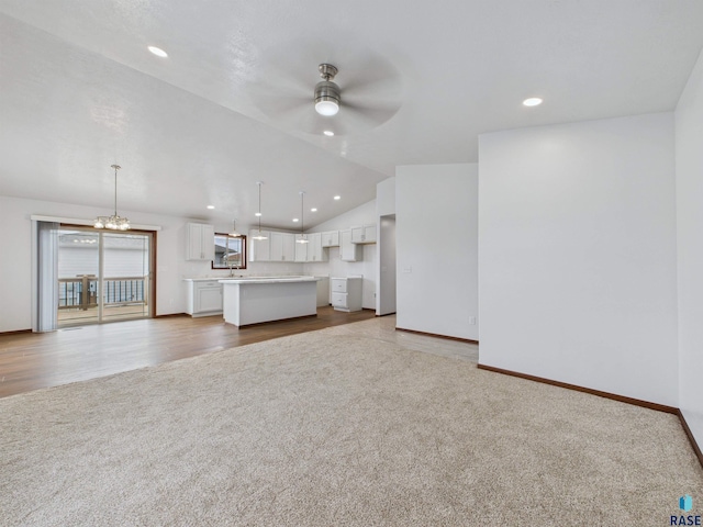 unfurnished living room with carpet floors, a sink, lofted ceiling, ceiling fan with notable chandelier, and recessed lighting