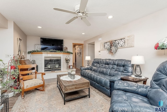living room with a textured ceiling, a fireplace, wood finished floors, recessed lighting, and a ceiling fan
