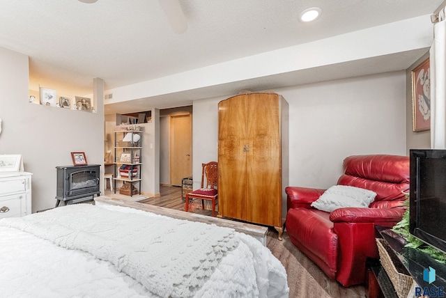 bedroom featuring a ceiling fan, wood finished floors, visible vents, and a wood stove