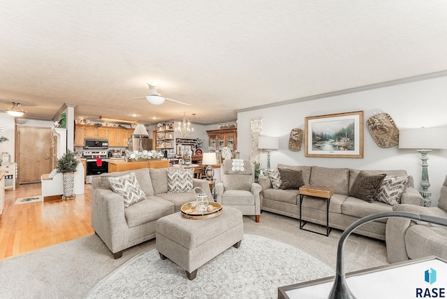 living room featuring ornamental molding, ceiling fan with notable chandelier, light wood-style floors, and a textured ceiling