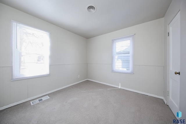 carpeted spare room featuring visible vents and wainscoting