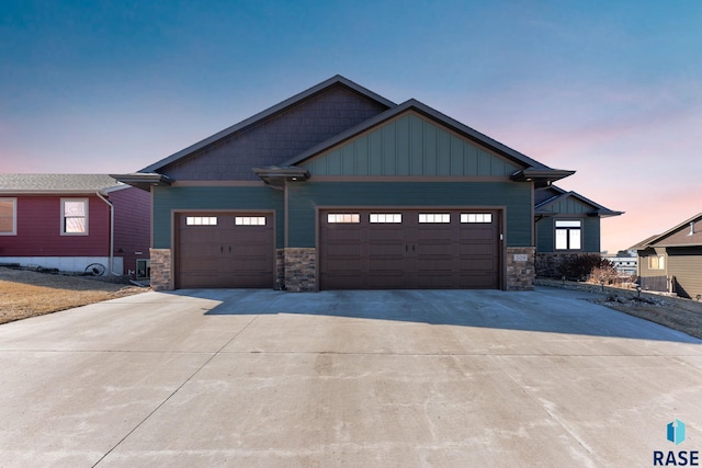 craftsman house with a garage, driveway, stone siding, and board and batten siding