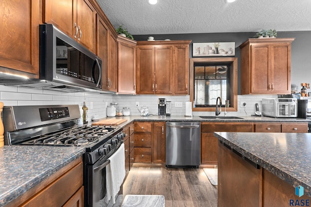 kitchen featuring tasteful backsplash, a textured ceiling, dark wood finished floors, stainless steel appliances, and a sink