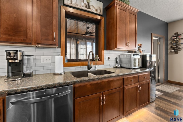kitchen featuring baseboards, a textured ceiling, stainless steel dishwasher, a sink, and wood finished floors