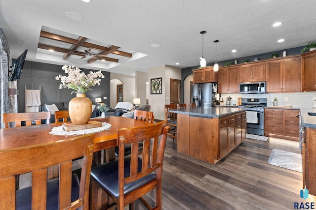 kitchen with dark wood-type flooring, arched walkways, a kitchen island, appliances with stainless steel finishes, and coffered ceiling