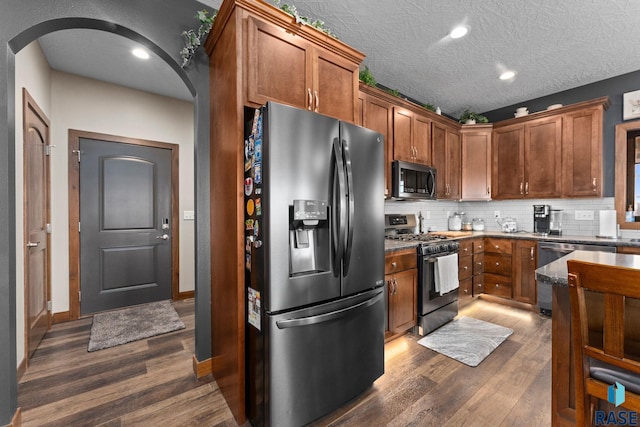 kitchen featuring arched walkways, appliances with stainless steel finishes, decorative backsplash, and dark wood-style flooring