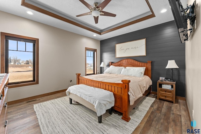 bedroom with a tray ceiling, visible vents, recessed lighting, hardwood / wood-style floors, and baseboards
