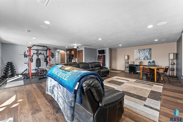 living area featuring dark wood-type flooring, arched walkways, a textured ceiling, visible vents, and recessed lighting