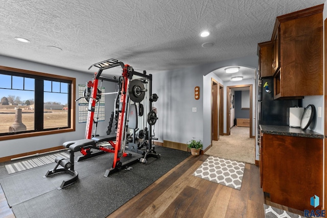 workout area with arched walkways, wood finished floors, baseboards, and a textured ceiling