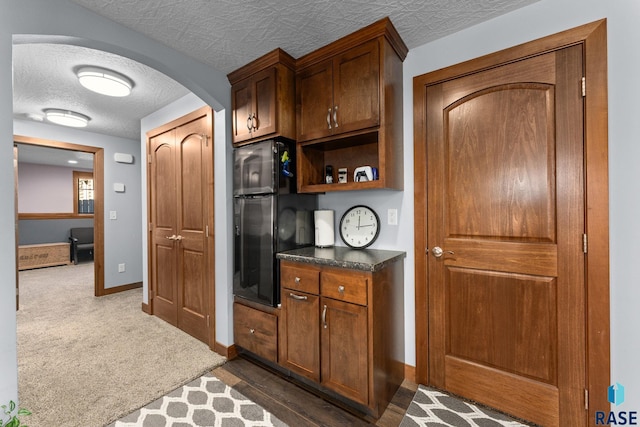 kitchen with baseboards, dark colored carpet, arched walkways, dark countertops, and a textured ceiling