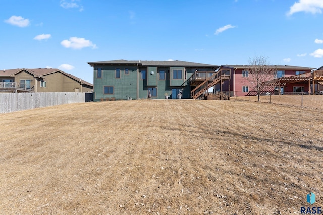 rear view of property featuring a yard, stairway, and fence