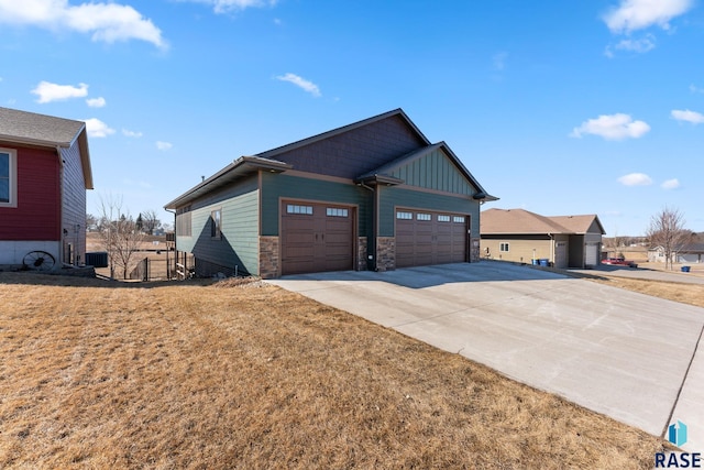 view of side of property featuring an attached garage, stone siding, board and batten siding, fence, and concrete driveway