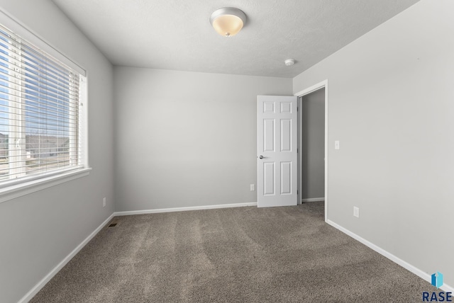 unfurnished room with a textured ceiling, baseboards, and carpet