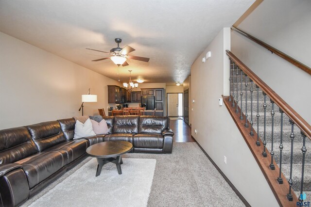 living room featuring carpet flooring, stairway, ceiling fan with notable chandelier, and baseboards