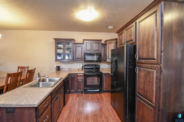 kitchen with a peninsula, light countertops, black appliances, dark wood-type flooring, and a sink