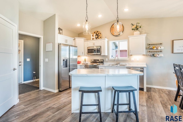 kitchen with white cabinets, a breakfast bar area, stainless steel appliances, a sink, and wood finished floors