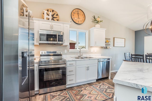 kitchen featuring vaulted ceiling, white cabinets, stainless steel appliances, a sink, and wood finished floors