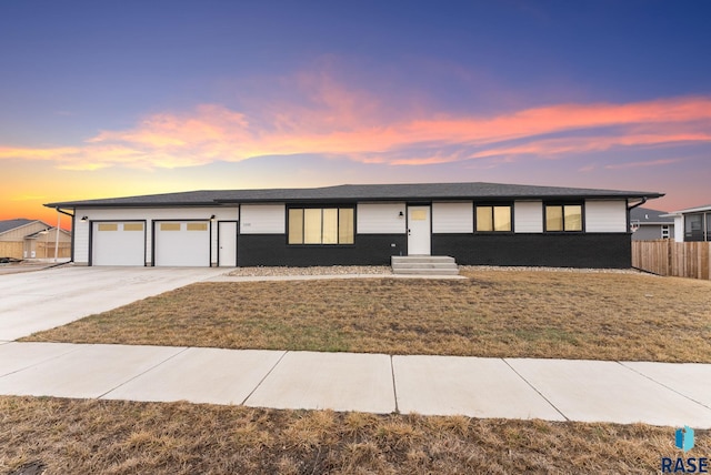 view of front of house with an attached garage, fence, a front lawn, and concrete driveway