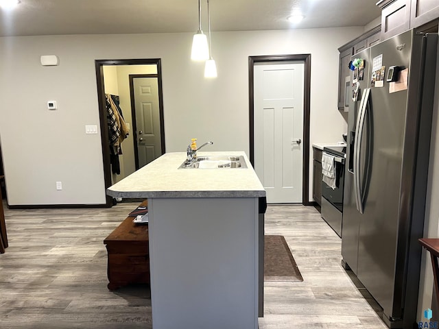 kitchen with light wood-style flooring, a sink, stainless steel fridge, range with electric stovetop, and a center island with sink