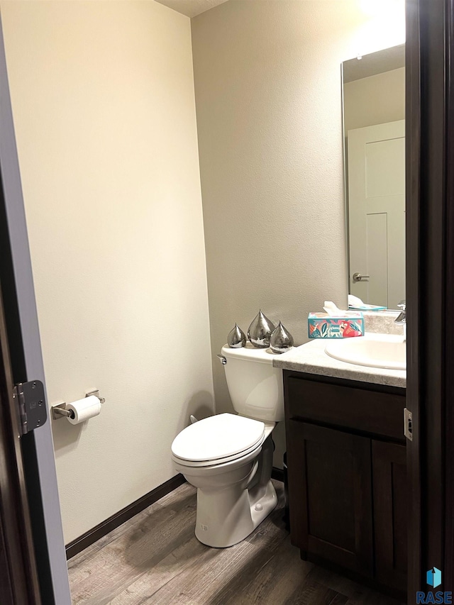 half bath featuring toilet, wood finished floors, vanity, and baseboards