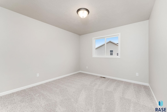 carpeted spare room with a textured ceiling, baseboards, and visible vents