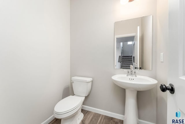 half bath featuring toilet, wood finished floors, and baseboards