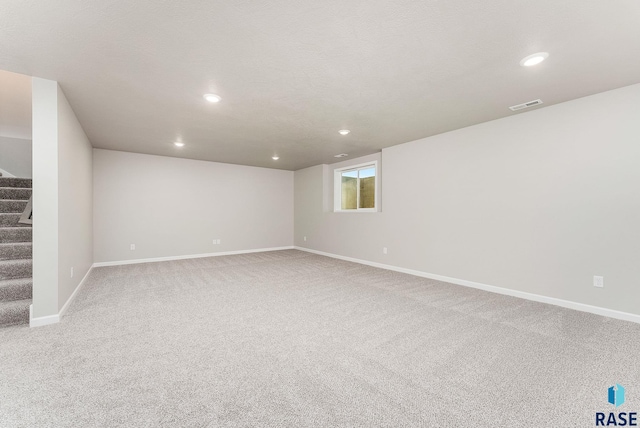 below grade area with baseboards, light carpet, recessed lighting, stairs, and visible vents